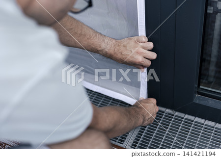 Person adjusting a mosquito screen on hook and loop tape on a window frame, illustrating home maintenance and practical DIY work. Person adjusting a mosquito screen on hook and loop tape on a window frame, illustrating home maintenance and practical DIY work. 141421194