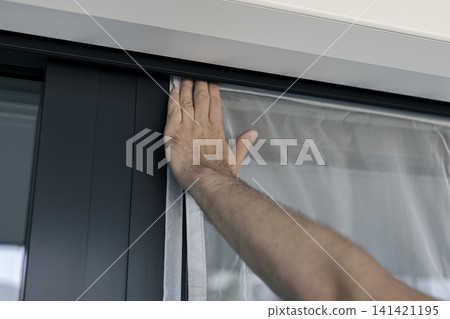 Hand pressing a white mosquito screen into the window frame, illustrating precise handwork and practical DIY maintenance. Hand pressing a white mosquito screen into the window frame, illustrating precise handwork and practical DIY maintenance. 141421195