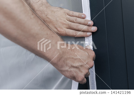 Hands adjusting a mosquito screen on hook and loop tape on a window frame, illustrating home maintenance and practical DIY work. 141421196