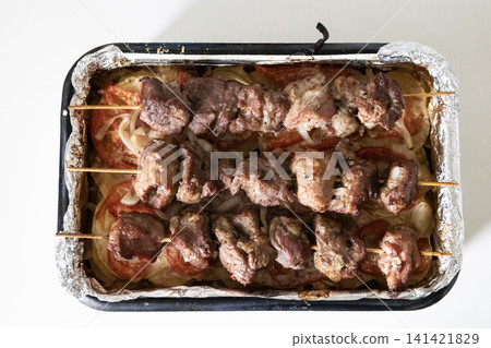 Baked meat skewers on wooden sticks placed in a baking tray over sliced tomatoes and onions, ready for serving delicious homemade barbecue meal, top view. Baked meat skewers on wooden sticks placed in a baking tray over sliced tomatoes and onions, ready for serving delicious homemade barbecue meal, top view. 141421829