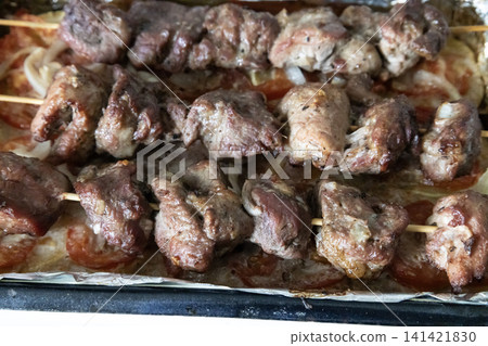 Baked meat skewers on wooden sticks placed in a baking tray over sliced tomatoes and onions, ready for serving delicious homemade barbecue meal, top view. Baked meat skewers on wooden sticks placed in a baking tray over sliced tomatoes and onions, ready for serving delicious homemade barbecue meal, top view. 141421830