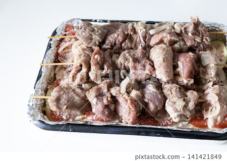 Raw marinated pork meat skewers on wooden sticks arranged in a baking tray with sliced tomatoes and onions, ready for cooking barbecue, top view. Raw marinated pork meat skewers on wooden sticks arranged in a baking tray with sliced tomatoes and onions, ready for cooking barbecue, top view. 141421849