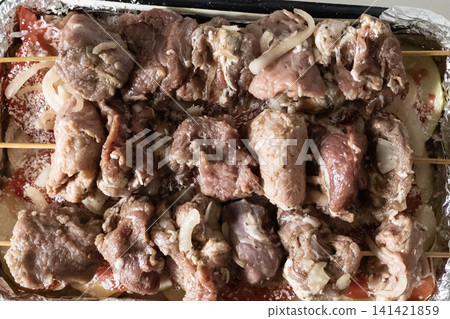 Raw marinated pork meat skewers on wooden sticks arranged in a baking tray with sliced tomatoes and onions, ready for cooking barbecue, top view. Raw marinated pork meat skewers on wooden sticks arranged in a baking tray with sliced tomatoes and onions, ready for cooking barbecue, top view. 141421859