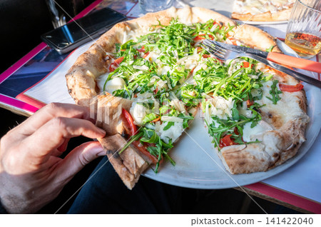 Naples, italy. December 30, 2024. Enjoying authentic neapolitan pizza topped with fresh arugula, mozzarella, and tomatoes, a classic italian culinary experience Naples, italy. December 30, 2024. Enjoying authentic neapolitan pizza topped with fresh arugula, mozzarella, and tomatoes, a classic italian culinary experience 141422040