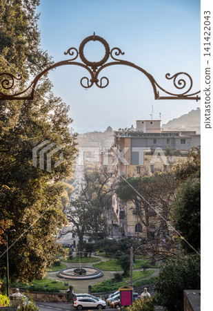 Naples, italy. December 30, 2024. Capodimonte park view of naples cityscape, seeing buildings, treelined street, and distant dome framed by an ornate iron arch Naples, italy. December 30, 2024. Capodimonte park view of naples cityscape, seeing buildings, treelined street, and distant dome framed by an ornate iron arch 141422043