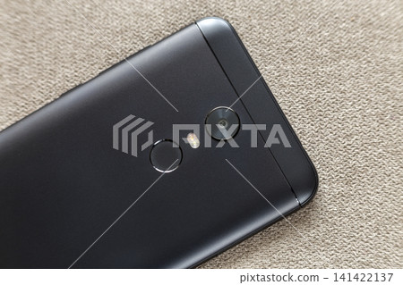 Back side of black cellphone isolated with security thumb fingerprint scanning device, camera and flash lighting on light cloth copy space background. Modern technology and smartphone design concept. 141422137