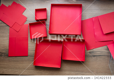 Lids from a red collapsible gift box gathered on a wooden table. Preparing a surprise. Lids from a red collapsible gift box gathered on a wooden table. Preparing a surprise. 141422333
