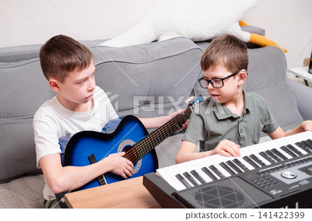 A boy with glasses and hearing aids plays the synthesizer with his older brother, who plays the guitar. The schoolboy has a hearing disability. A boy with glasses and hearing aids plays the synthesizer with his older brother, who plays the guitar. The schoolboy has a hearing disability. 141422399