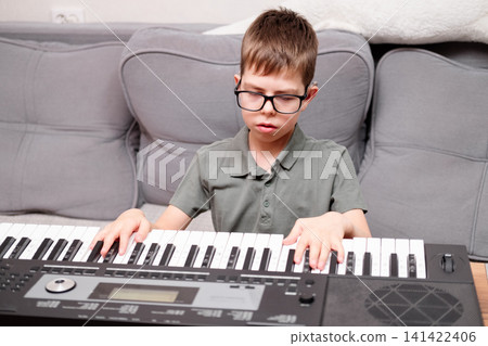 A boy with glasses and hearing aids is learning to play the synthesizer. The schoolchild has a hearing disability. A boy with glasses and hearing aids is learning to play the synthesizer. The schoolchild has a hearing disability. 141422406