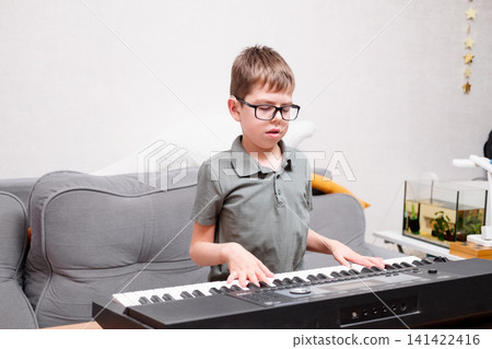 A boy with glasses and hearing aids is learning to play the synthesizer. The schoolchild has a hearing disability. A boy with glasses and hearing aids is learning to play the synthesizer. The schoolchild has a hearing disability. 141422416