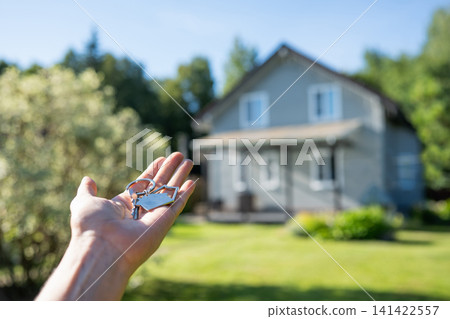 Hand holding house keys in front of blurred home Hand holding house keys in front of blurred home 141422557