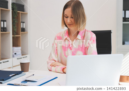 Young businesswoman smiling as she works on a laptop sitting in an modern office Young businesswoman smiling as she works on a laptop sitting in an modern office 141422893