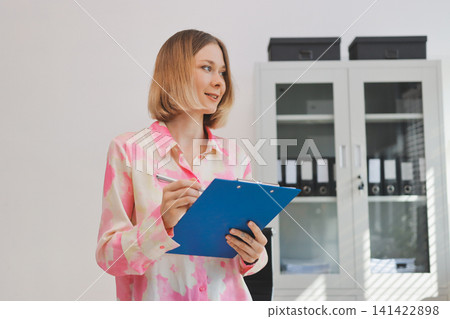 Young businesswoman smiling as she works on a laptop sitting in an modern office Young businesswoman smiling as she works on a laptop sitting in an modern office 141422898