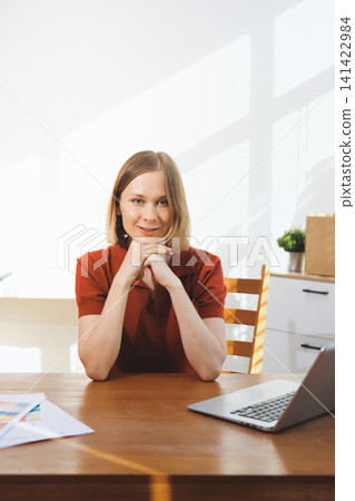 Young woman works on a touchpad, feeling comfortable at cozy home office with a green plant on the background 141422984