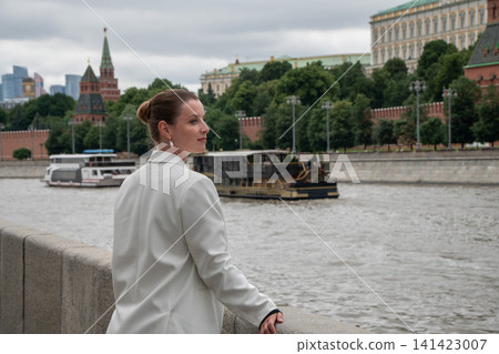Woman glances back beside Moscow River on Sofiyskaya Embankment with Kremlin skyline in background. Urban travel, leisure, architecture, riverfront, tourism, modern lifestyle, freedom Woman glances back beside Moscow River on Sofiyskaya Embankment with Kremlin skyline in background. Urban travel, leisure, architecture, riverfront, tourism, modern lifestyle, freedom 141423007