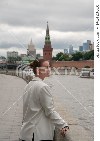 Woman looks back while walking along Sofiyskaya Embankment in Moscow with Kremlin across river. Urban lifestyle, travel, city exploration, confidence, architecture, sightseeing, leisure Woman looks back while walking along Sofiyskaya Embankment in Moscow with Kremlin across river. Urban lifestyle, travel, city exploration, confidence, architecture, sightseeing, leisure 141423010