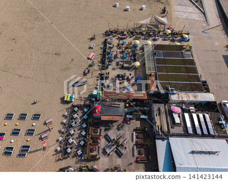 Beautiful top down high altitude aerial panoramic perspective of seaside beach clubs with outdoor patio terraces wooden furniture sunbeds and green roofs under bright sunlight Beautiful top down high altitude aerial panoramic perspective of seaside beach clubs with outdoor patio terraces wooden furniture sunbeds and green roofs under bright sunlight 141423144