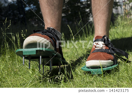 Person walking in sneakers with spiked aerator shoes, illustrating efficient lawn care tools and soil treatment for home yards. Person walking in sneakers with spiked aerator shoes, illustrating efficient lawn care tools and soil treatment for home yards. 141423175