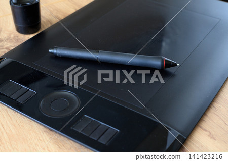 Digital stylus rest on a black graphics tablet for digital drawing. Digital illustration process concept. Digital stylus rest on a black graphics tablet for digital drawing. Digital illustration process concept. 141423216