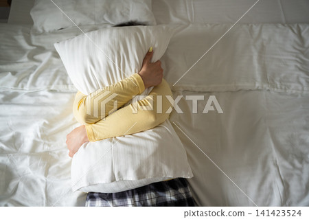 Person embracing a pillow on a bed suggesting emotional comfort and stress relief. Sleep wellness mental health and relaxation concept Person embracing a pillow on a bed suggesting emotional comfort and stress relief. Sleep wellness mental health and relaxation concept 141423524
