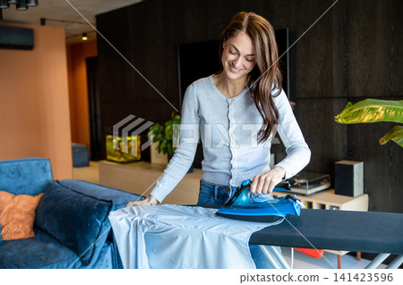 Pretty smiling woman feeling contented while doing ironing Pretty smiling woman feeling contented while doing ironing 141423596