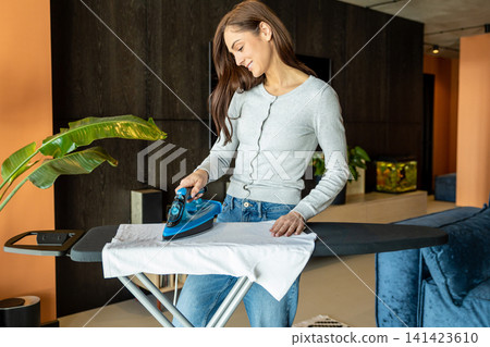 Woman in jeans doing housework and ironing clothes Woman in jeans doing housework and ironing clothes 141423610