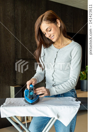 Woman in jeans doing housework and ironing clothes Woman in jeans doing housework and ironing clothes 141423611