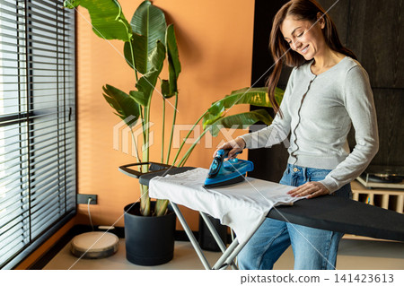 Young woman ironing clothes at home while standing at the ironing board Young woman ironing clothes at home while standing at the ironing board 141423613
