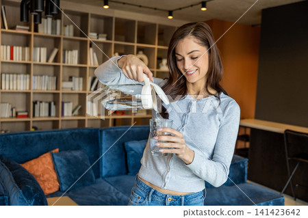 Young woman pouring water from the jar to the glass Young woman pouring water from the jar to the glass 141423642