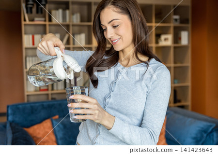 Young woman pouring water from the jar to the glass 141423643
