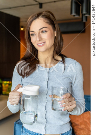 Young woman pouring water from the jar to the glass Young woman pouring water from the jar to the glass 141423644