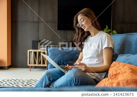 Smiling young woman with laptop in hands sitting on a sofa Smiling young woman with laptop in hands sitting on a sofa 141423673
