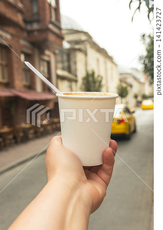 First person POV view of a hand holding a white paper cup filled with hot traditional Turkish salep drink with cinnamon on a blurry Istanbul street background, vertical First person POV view of a hand holding a white paper cup filled with hot traditional Turkish salep drink with cinnamon on a blurry Istanbul street background, vertical 141423727