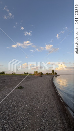 Still beach scene with gravel and water under serene clouds Still beach scene with gravel and water under serene clouds 141423886