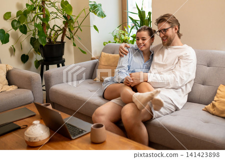 Cute young couple sitting on the sofa at home and feeling peaceful and relaxed Cute young couple sitting on the sofa at home and feeling peaceful and relaxed 141423898