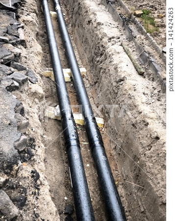 Laying new underground plastic pipes in an earth trench. Laying new underground plastic pipes in an earth trench. 141424263