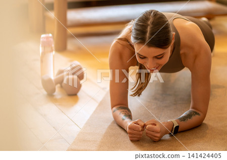 Young fitness coach holding low plank on mat 141424405