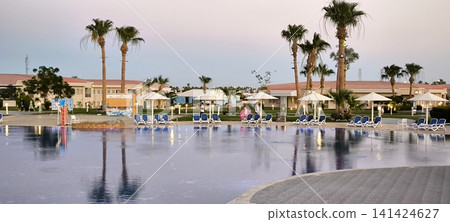 Magical sunset over a resort pool with palm trees and umbrellas 141424627