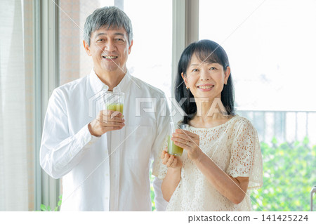 一對老年夫婦面帶微笑地喝著綠色果汁。 141425224
