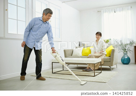 A smiling man and a woman in her 60s vacuum while chatting. A smiling man and a woman in her 60s vacuum while chatting. 141425852