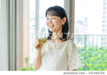 A woman drinking green juice with a smile A woman drinking green juice with a smile 141426150