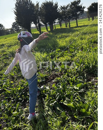 A girl walks across a green meadow, balancing with her arms outstretched - playing outdoors in nature. A girl walks across a green meadow, balancing with her arms outstretched - playing outdoors in nature. 141426276