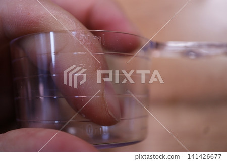 Hand Holding Measuring Cup with Volume Markings Hand Holding Measuring Cup with Volume Markings 141426677
