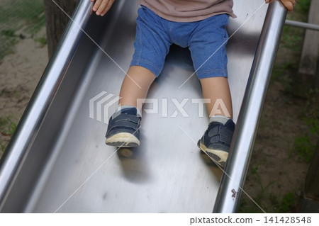 公園裡，一個穿著短褲的孩子正從溜滑梯上滑下來，露出他的腳。 141428548