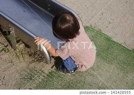 The back view of a child in a short-sleeved shirt sitting and playing at the exit of a slide. The back view of a child in a short-sleeved shirt sitting and playing at the exit of a slide. 141428555