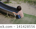 A child in a short-sleeved shirt sits and plays at the exit of the slide. 141428556