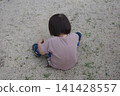 The back view of a child sitting on the ground in a park, playing in the sand. 141428557