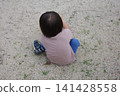 The back view of a child sitting on the ground in a park, playing in the sand. 141428558