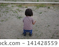 A toddler's back as they crouch down and play in the sand on the park ground. 141428559