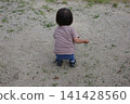 A toddler's back as they crouch down and play in the sand on the park ground. 141428560